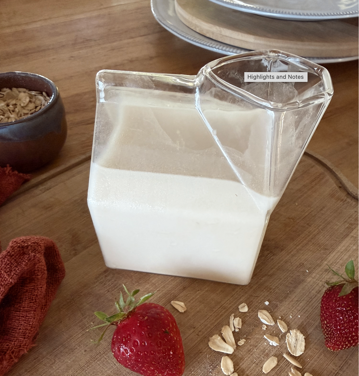 Glass bottle of creamy homemade oat milk next to a small glass and scattered whole oats on a linen surface
